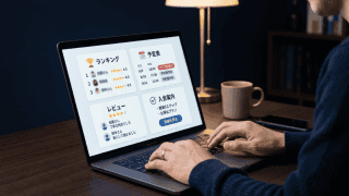 デスクでノートパソコンを操作する男性の手元。画面にはランキング、予定表、レビュー、入会案内が表示されている。